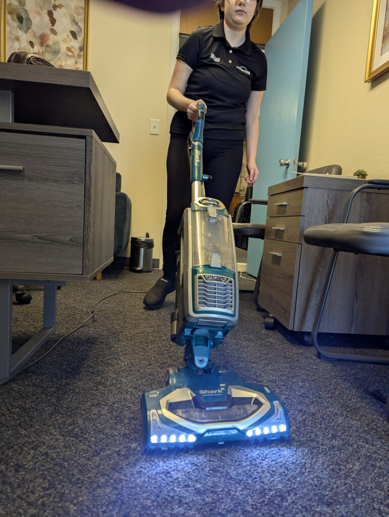 carpet cleaning being performed with a blue shark vacuum by a woman in a professional shirt