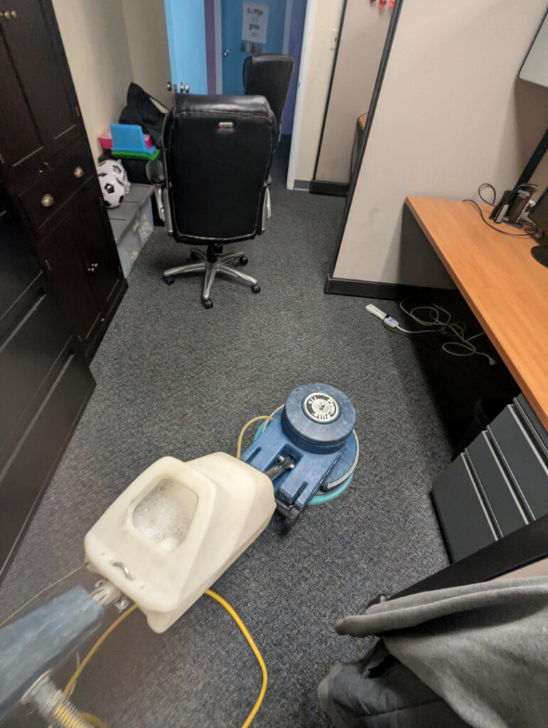 carpet cleaning in an office space using a rotary extractor machine with soapy water and a hose connected