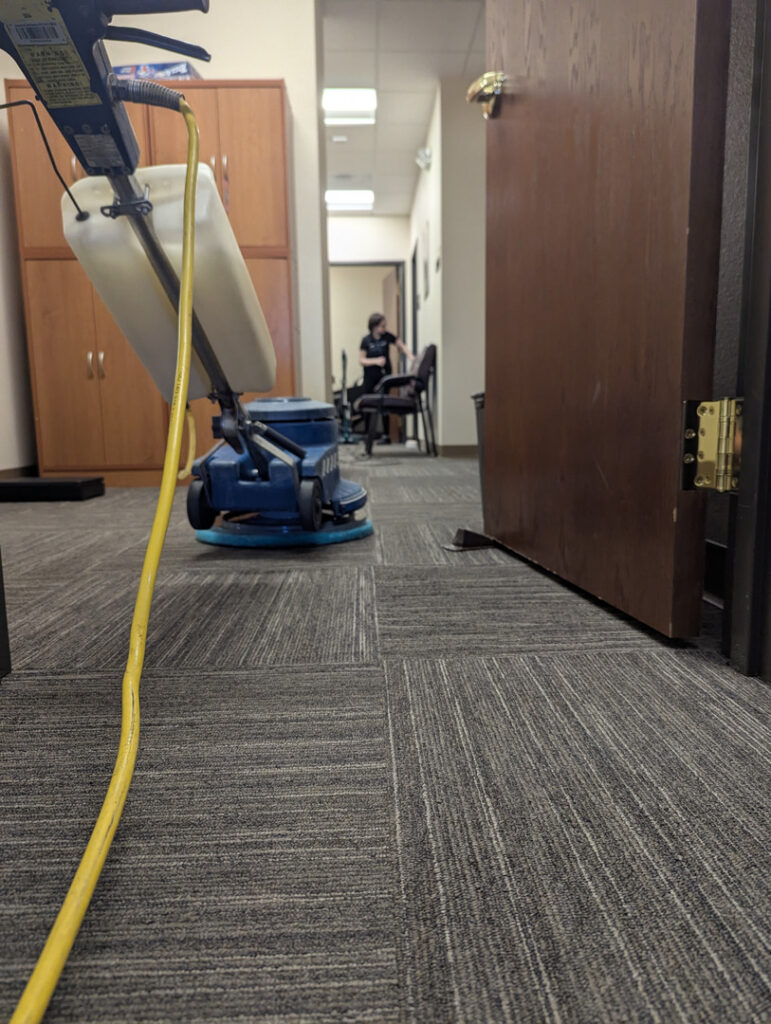 carpet cleaning in an office using a rotary cleaning machine and visible yellow power cord on the floor