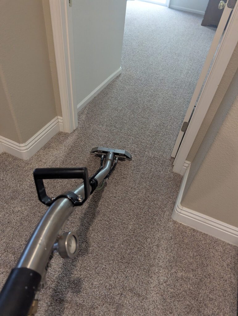 crystal clean carpet pros cleaning a light gray carpet with a carpet cleaning machine in a well-lit hallway