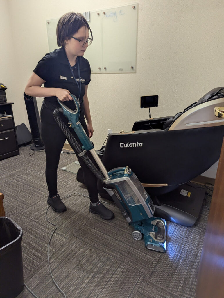 crystal clean carpet pros cleaning carpet with a vacuum in an office setting while standing next to a chair