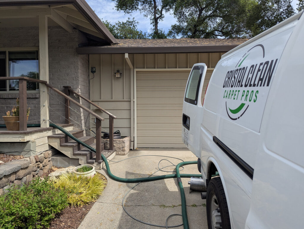 crystal clean carpet pros providing carpet cleaning services with hoses connected to a work van and a residential entrance