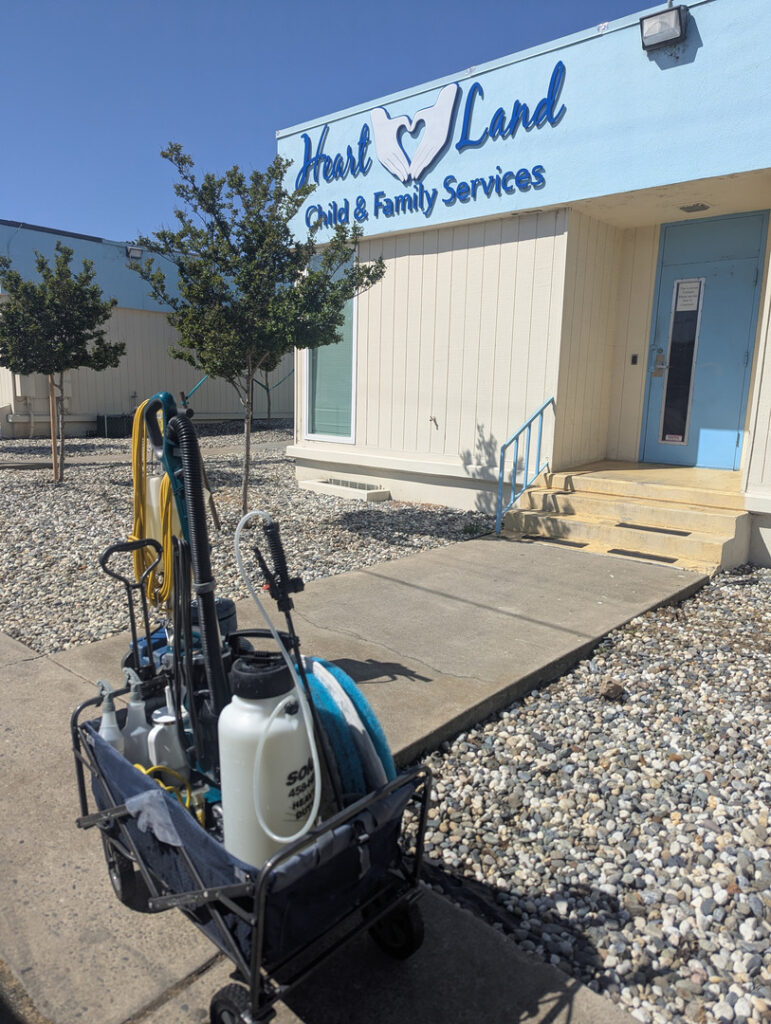 equipment cart with cleaning supplies and tools near a building entrance with gravel landscaping and trees