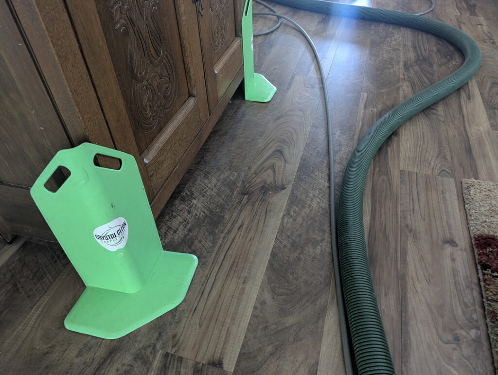 green equipment for carpet cleaning hoses positioned on a wooden floor near furniture