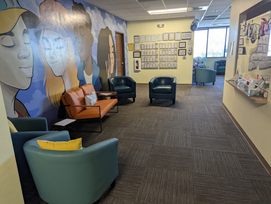 waiting area with blue and orange chairs and a mural on the wall featuring illustrated faces and decorative elements