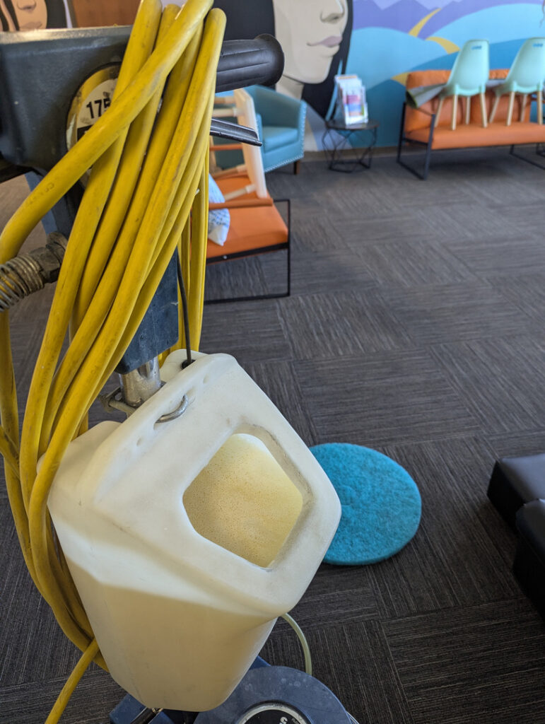 yellow hose coiled next to a machine with foamy liquid container indicating carpet cleaning services in a modern setting